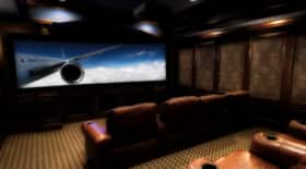 This is a picture of a home theater setup in someones basement. There are chairs/couches and a big flat screen TV setup.